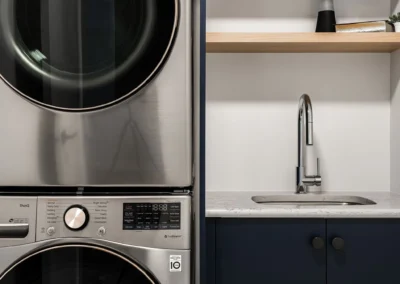 small laundry sink area with navy cabinets, open shelf and upper storage by Saskatoon basement developer Axium Interiors